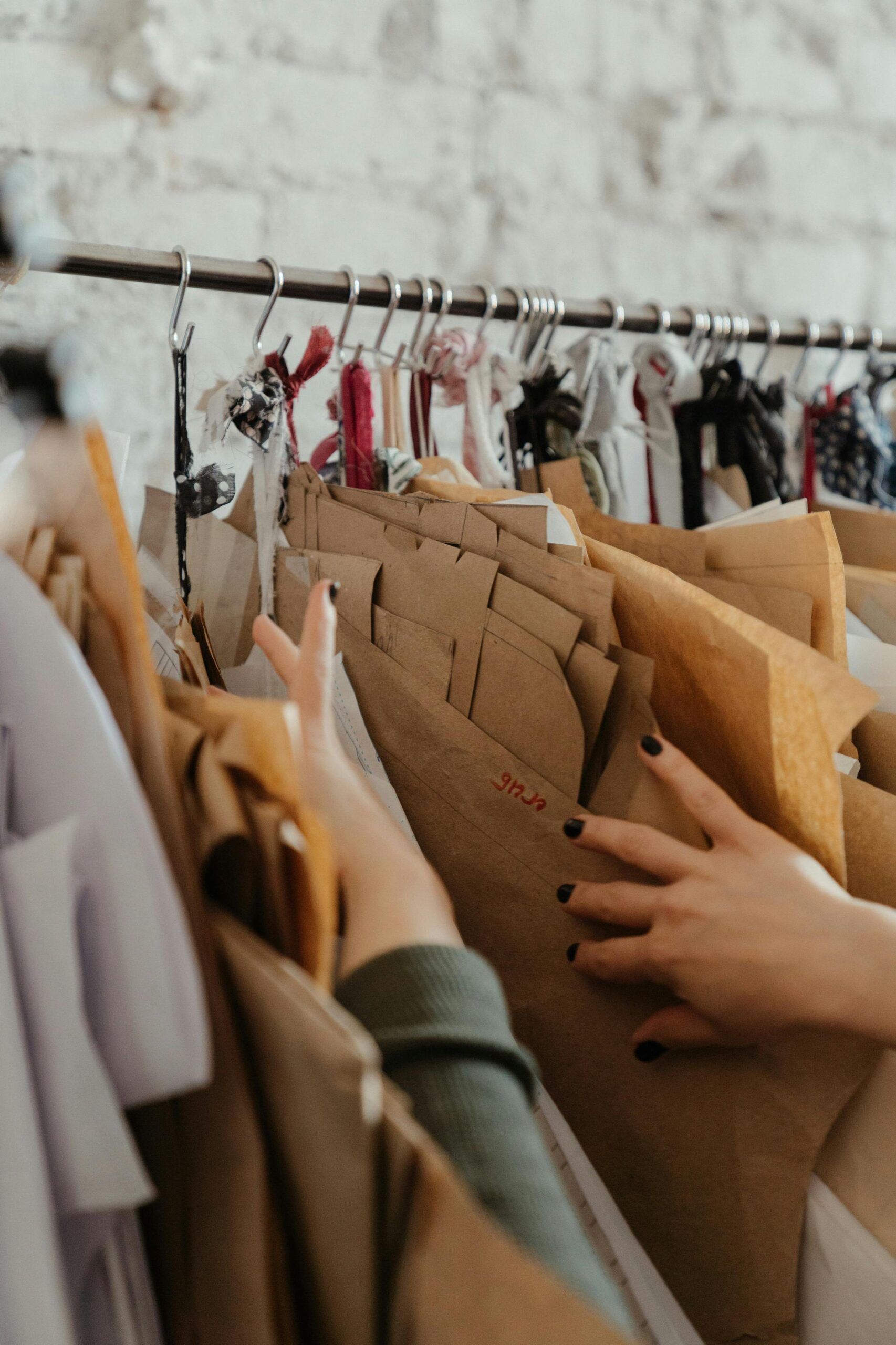 Close-up of hands sorting assorted sewing patterns on a rack in a fashion design studio.